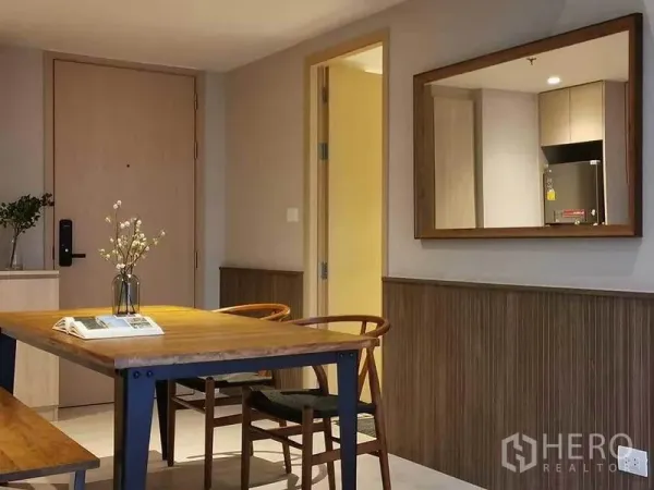 Condominium for rent in Bang Rak, Bangkok - Wood dining table with chairs and bench next to a large wall mirror reflecting the compact kitchen.