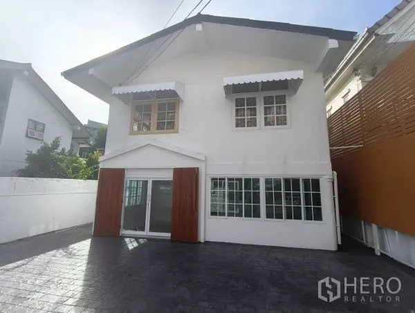 บ้าน ให้เช่าในBang Na, Bangkok - ด้านหน้าบ้านเดี่ยวสองชั้นสีขาวในย่านบางนา ประตูบานเลื่อน กระจก กันสาด และลานจอดรถปูพื้นกว้าง