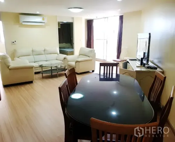 Condominium for rent in Watthana, Bangkok - Bright open-plan living and dining room with cream leather sofa set, glass coffee table, wooden dining table, TV console and balcony doors.