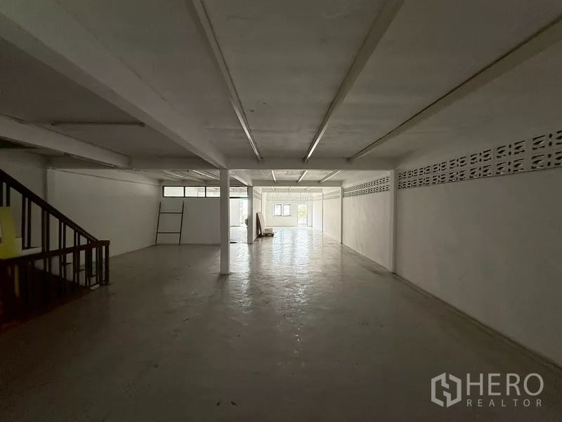 Shophouse for rent - Long open workspace with low windows and a rear staircase.