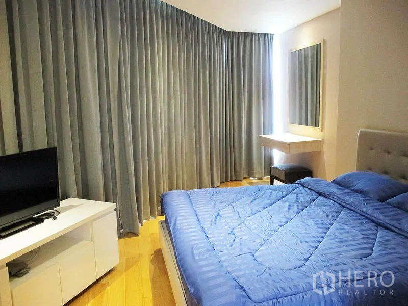 Condominium for rent in Watthana, Bangkok - Master bedroom with blue duvet, floor-to-ceiling curtains, wall mirror and TV console.