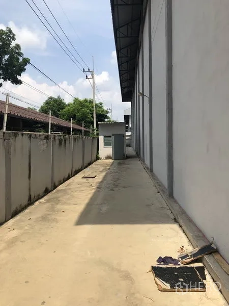 Factory for rent in Lam Luk Ka, Pathum Thani - Narrow service walkway along the building with perimeter wall and utility box.