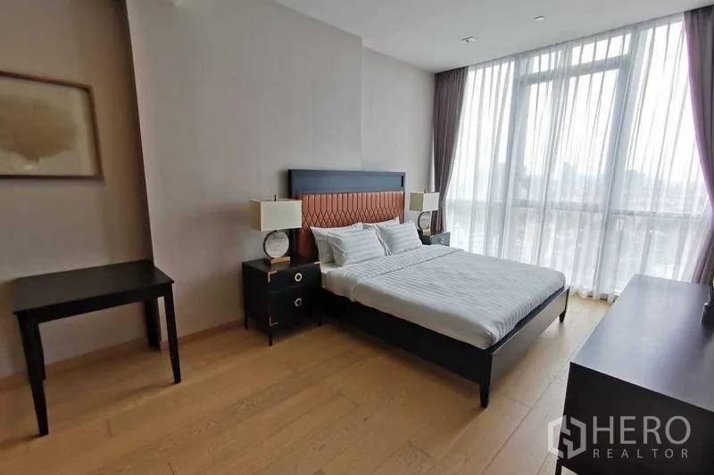 Condominium for rent or sale in Watthana, Bangkok - Bedroom with double bed, side tables and a large window with sheer curtains.