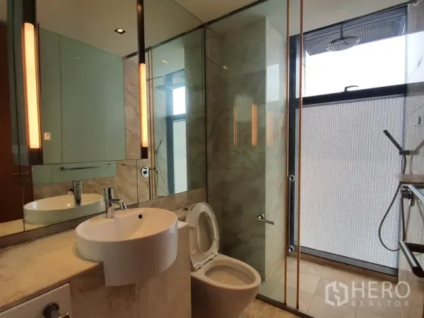 Condominium for rent in Sathon, Bangkok - Modern bathroom with marble finishes, round basin and glass-enclosed rain shower beside a frosted window.