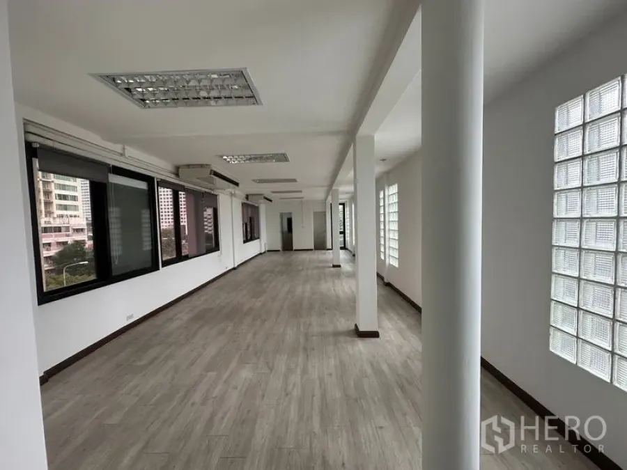 Office Space for rent in Sathon, Bangkok - Long rectangular office floor with columns, glass-block wall, fluorescent ceiling lights and blackout blinds.