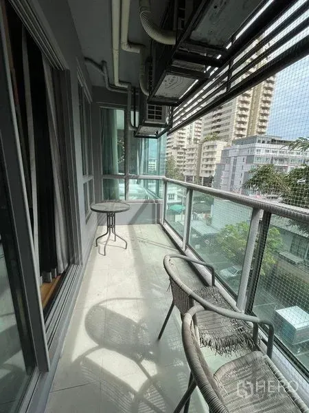 Condominium for rent in Watthana, Bangkok - Long balcony with glass railing, bistro table and chairs, overlooking mid-rise city buildings.
