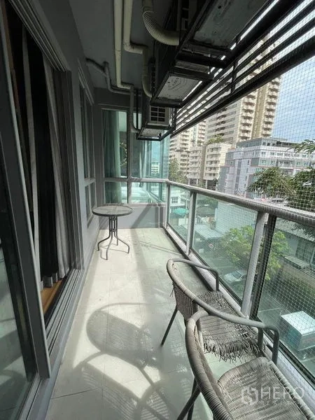 Condominium for rent in Watthana, Bangkok - Long balcony with glass railing, bistro table and chairs, overlooking mid-rise city buildings.
