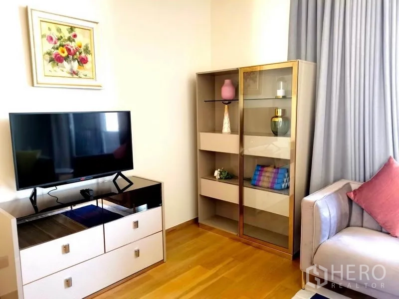 Condominium for rent in Khlong Toei, Bangkok - Compact living corner with flat-screen TV, display cabinet, and pastel sofa.