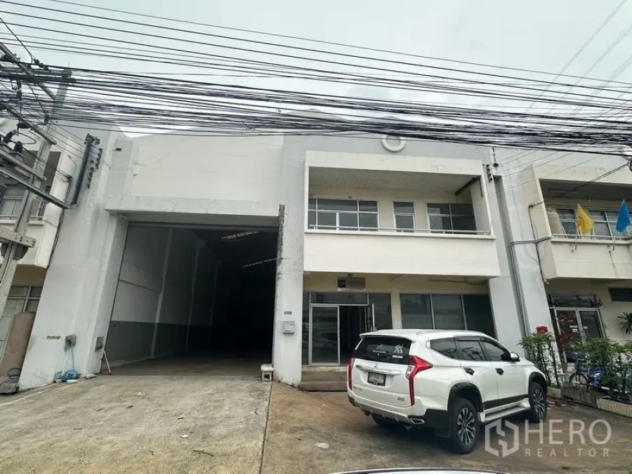 Factory for rent in Khlong Luang, Pathum Thani - Street-side view of the factory front with driveway and a parked SUV.