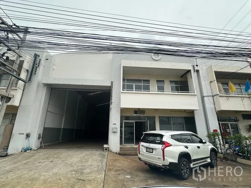 Factory for rent in Khlong Luang, Pathum Thani - Street-side view of the factory front with driveway and a parked SUV.