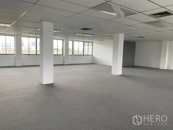Office Space for rent in Ratchathewi, Bangkok - Spacious empty office zone with white pillars, neutral carpeting, and city views through the windows.