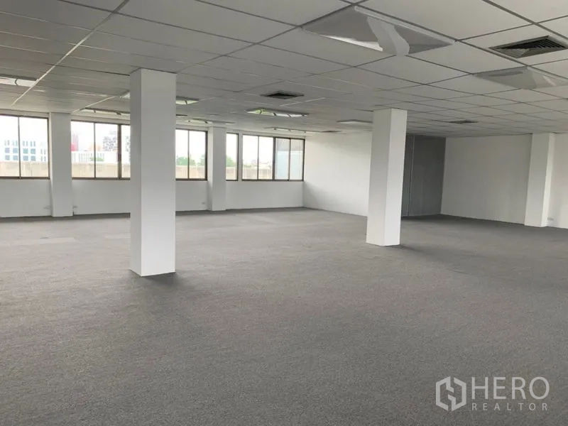 Office Space for rent in Ratchathewi, Bangkok - Spacious empty office zone with white pillars, neutral carpeting, and city views through the windows.