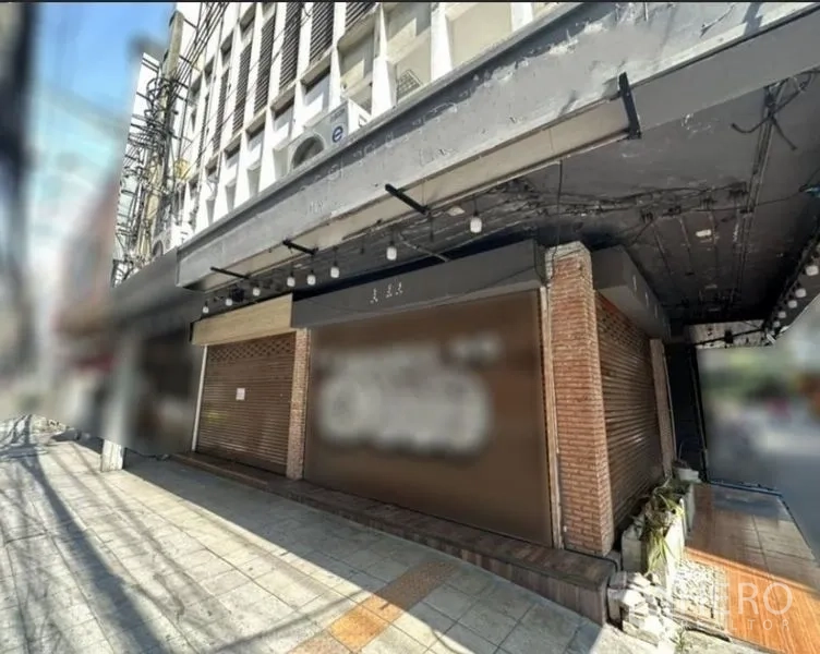 Shophouse for rent in Khlong Toei, Bangkok - Street-level view of a Bangkok shophouse facade with closed roller shutters, brick pillars and a shaded sidewalk.