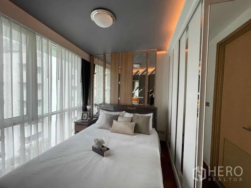 Condominium for sale in Watthana, Bangkok - Corner bedroom with sheer curtains, mirrored headboard feature wall and built-in wardrobes.