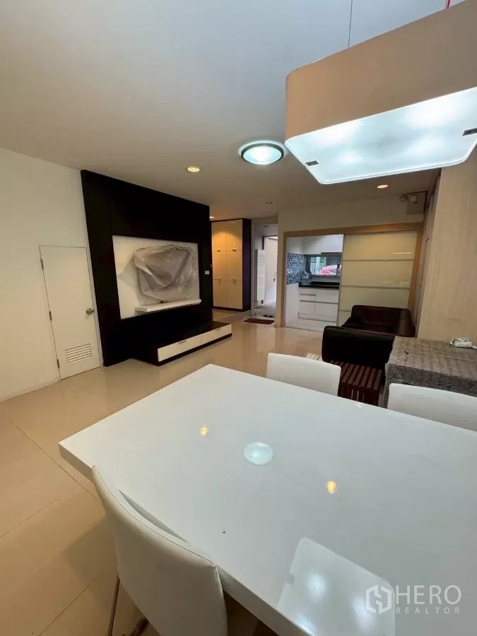 Townhouse for rent in Suan Luang, Bangkok - Open-plan dining and living area with built-in TV wall and view to the kitchen.