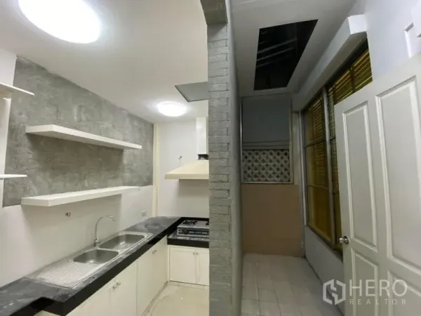 Townhouse for rent in Lat Phrao, Bangkok - Compact kitchen with double sink, stone-style backsplash, open shelves, gas hob and range hood.