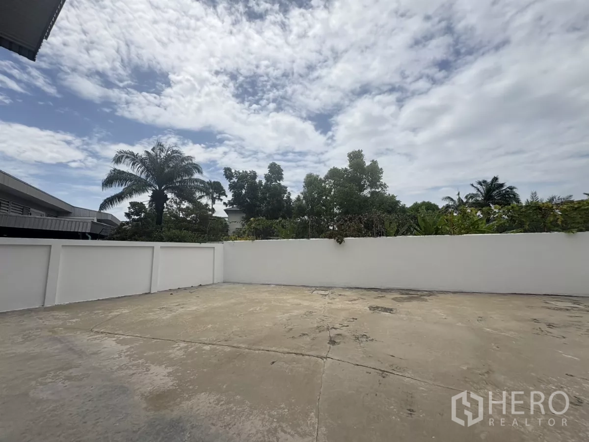 Factory for rent in Phra Samut Chedi, Samut Prakan - Private concrete yard with white perimeter wall and tropical trees beyond.