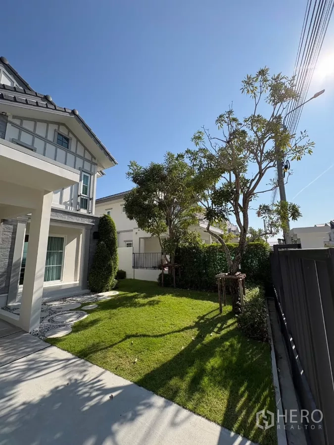 Detached House for rent in Bang Phli, Samut Prakan - Lawn and driveway beside the house with mature trees and neat landscaping.