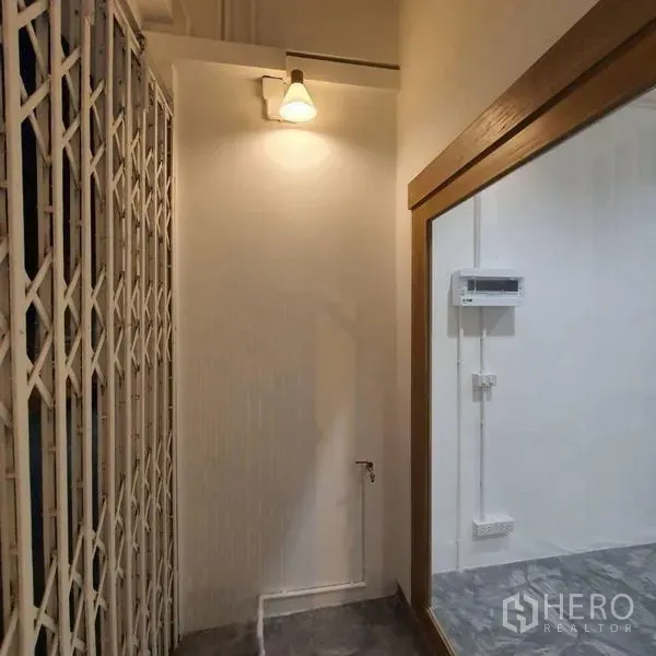 Shophouse for rent or sale in Khlong Toei, Bangkok - Entrance corner showing security folding gate, wall light and interior glass window.