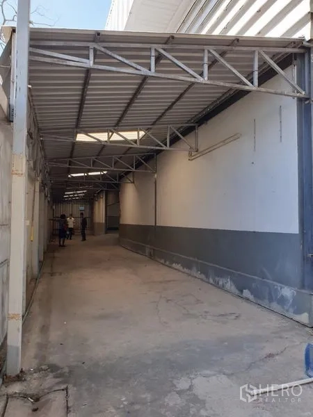 Warehouse for rent in Lam Luk Ka, Pathum Thani - Long covered service corridor along the warehouse wall with metal roofing.