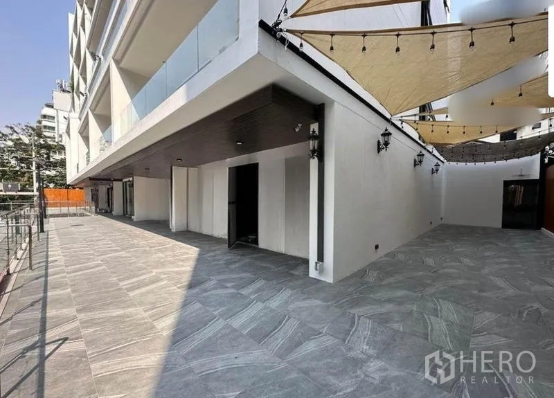 零售空间 出租 - 一层超大露台，灰色地砖、遮阳篷与宽阔门面，位于现代化建筑下方。