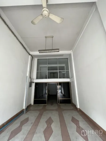 店屋 出租在Phra Khanong, Bangkok - 临街商铺一层，挑高空间，吊扇与几何地砖，前方玻璃夹层隔间。