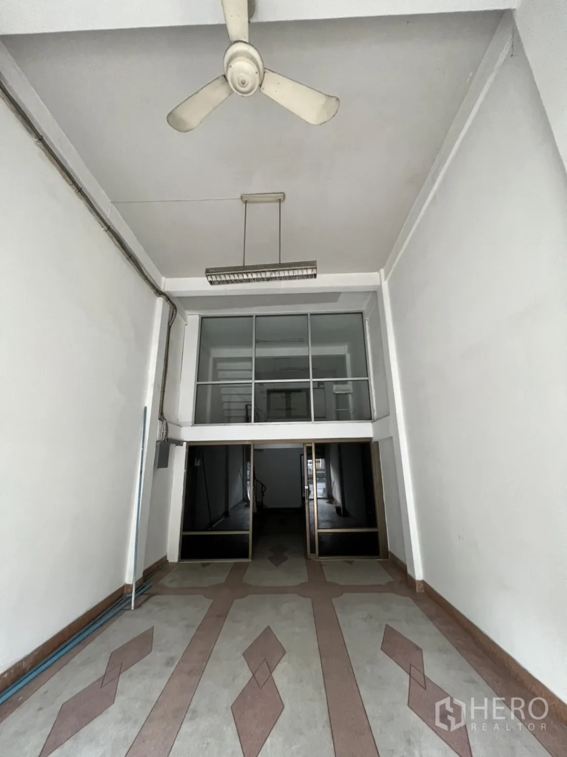 Shophouse for rent in Phra Khanong, Bangkok - Empty shophouse ground floor with high ceiling, ceiling fan, patterned floor and glass mezzanine wall.