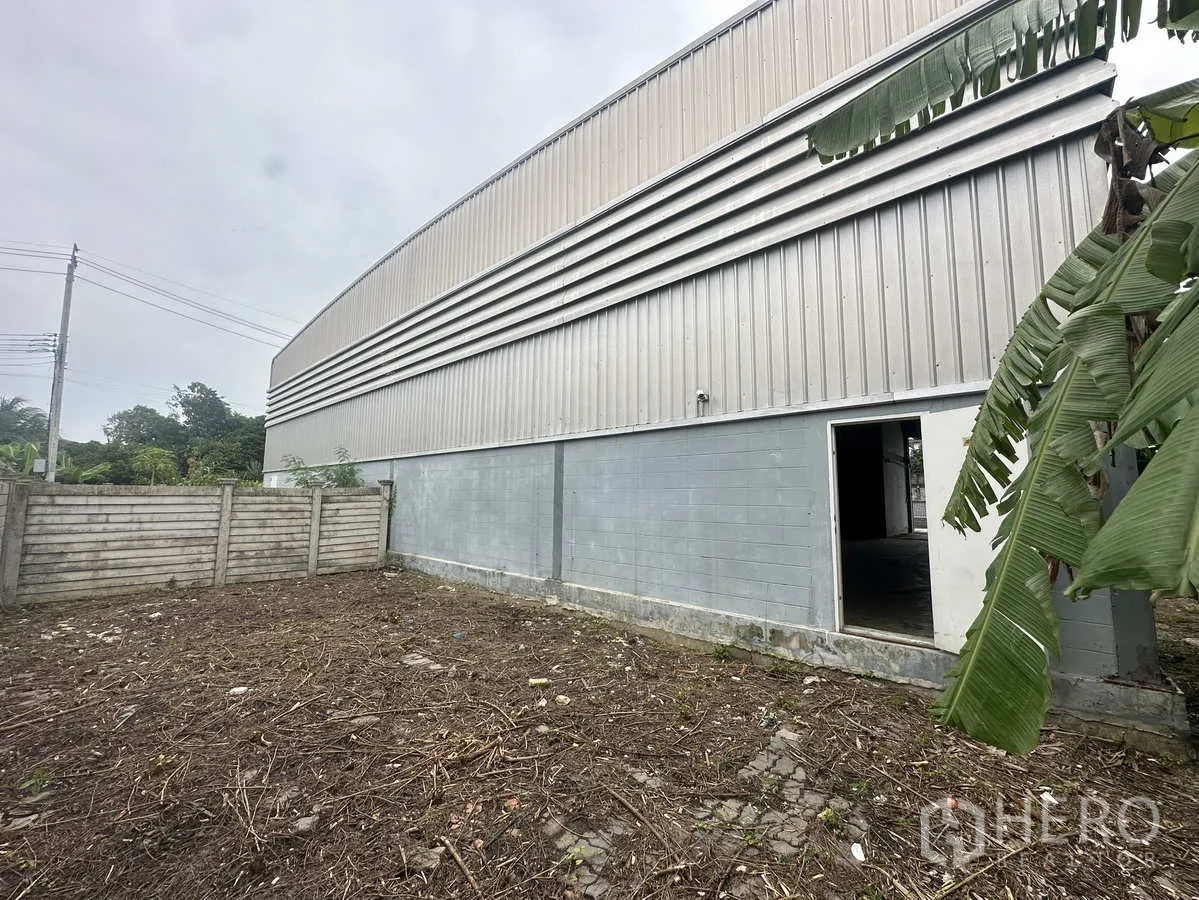 Warehouse for rent or sale in Bang Yai, Nonthaburi - Side yard next to corrugated metal wall of the warehouse with a side access door.