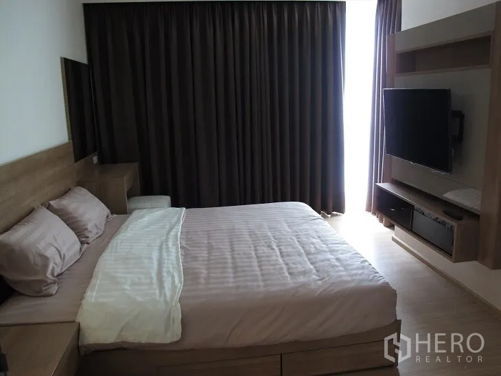Condominium for rent or sale in Khlong Toei, Bangkok - Primary bedroom featuring a king bed, dark curtains, and TV unit in warm wood tones.