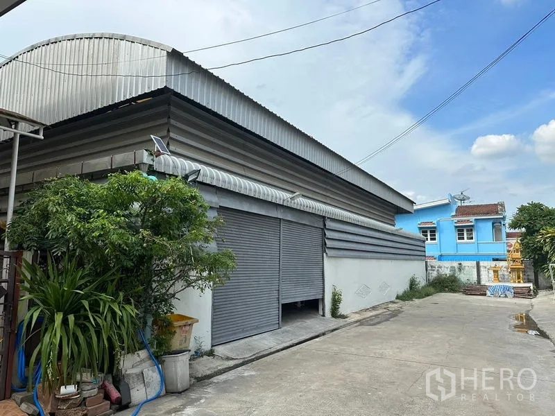 Warehouse for rent in Bueng Kum, Bangkok - Warehouse exterior with wide rolling shutter doors and corrugated metal roof.
