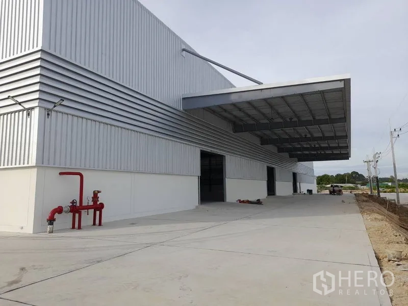 โรงงาน ให้เช่าในMueang Rayong, Rayong - ด้านหน้าโรงงานสมัยใหม่ ผนังเมทัลชีท ชายคาโหลดสินค้าขนาดใหญ่ ลานคอนกรีตกว้าง และท่อดับเพลิงสีแดง