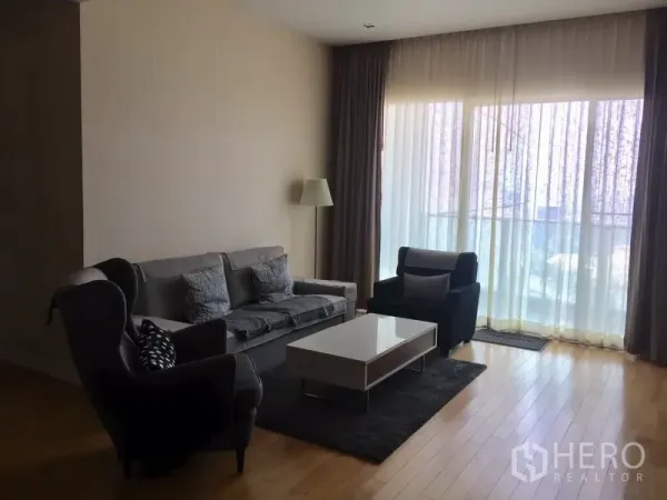 Condominium for rent in Khlong Toei, Bangkok - Bright living room with hardwood floors, sofa set, armchairs, coffee table and floor-to-ceiling curtains.