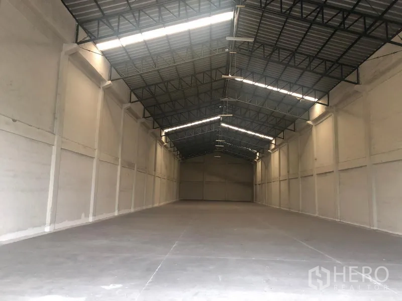 Warehouse for rent in Pathum Thani - Empty warehouse interior with high steel truss roof, skylights and smooth concrete floor.