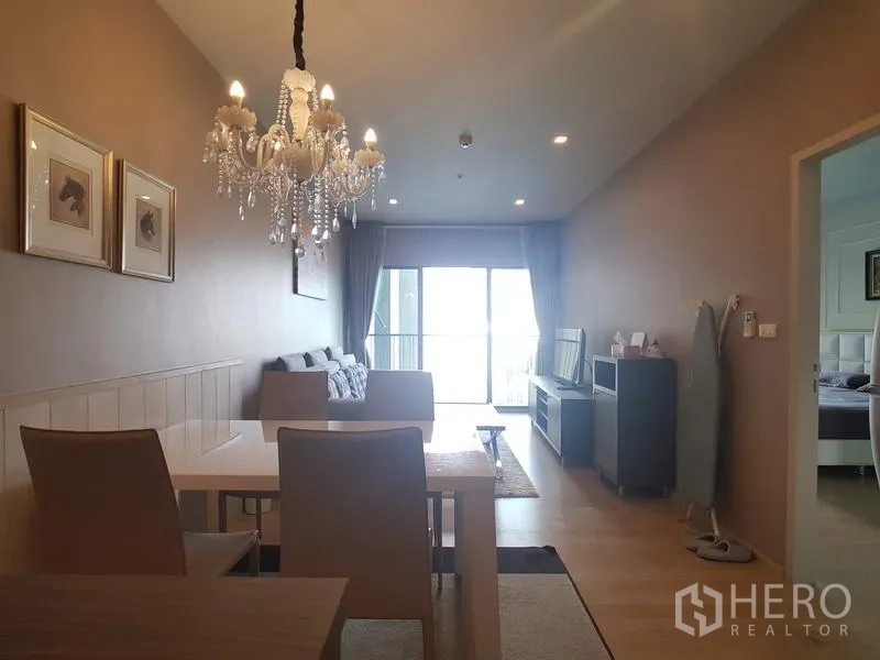 Condominium for rent in Bangkok - Dining space under a crystal chandelier facing the living area and balcony beyond.