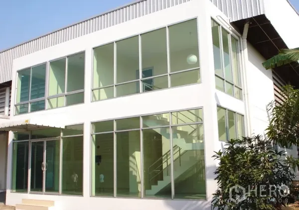 Warehouse for rent in Samut Prakan - Two-storey glass-front office attached to the warehouse with staircase and landscaped entry.