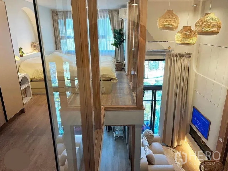 Condominium for rent in Huai Khwang, Bangkok - Glass walkway linking mezzanine rooms overlooking a double-height living room with TV and woven pendant lights.