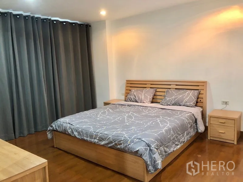 公寓 出租或出售在Watthana, Bangkok - 宽敞卧室，木质床架与灰色床品，厚窗帘与暖色灯光