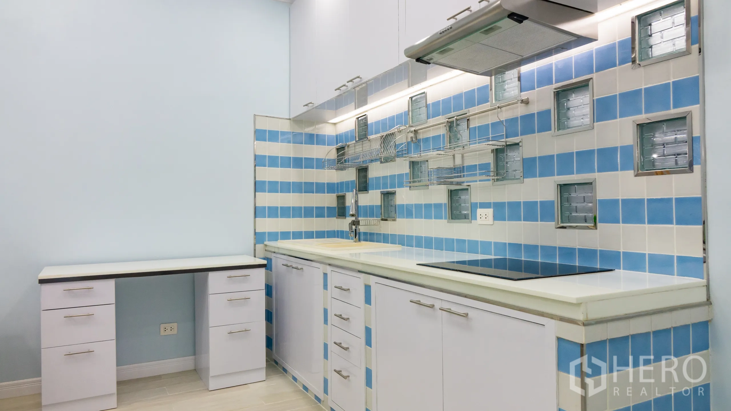 Condominium for rent or sale in Khlong Toei, Bangkok - Modern kitchen with induction cooktop, range hood and blue‑and‑white tiled backsplash.