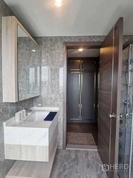 คอนโด ขายในHuai Khwang, Bangkok - ห้องน้ำที่สองพร้อมเคาน์เตอร์อ่างล้างหน้า กระจกบานใหญ่ กระเบื้องสีเทา และประตูสู่ห้องแต่งตัว