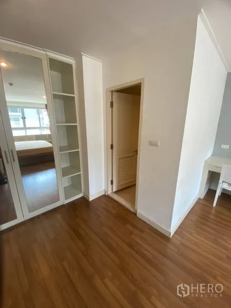 Condominium for rent in Watthana, Bangkok - Bedroom entry showing built-in mirrored wardrobe, open shelving, and wood floors.