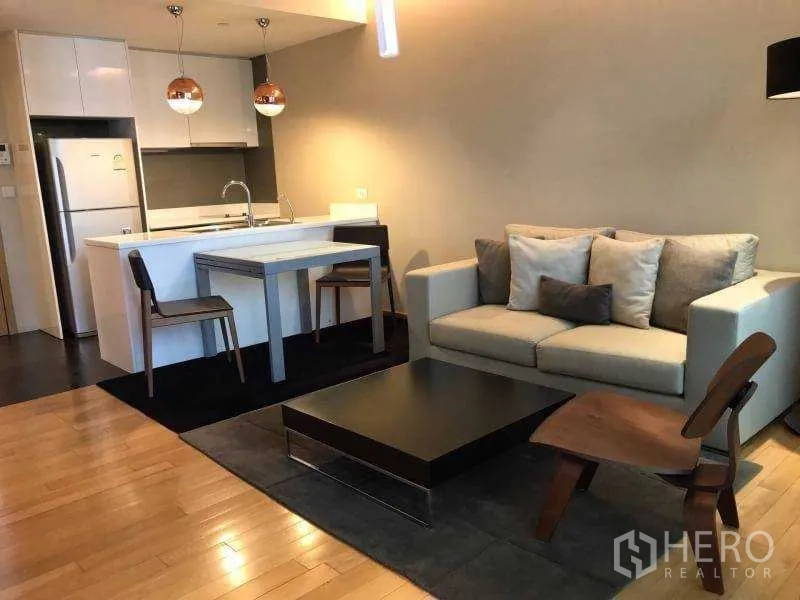 Condominium for rent in Watthana, Bangkok - Modern living room with sofa, dining set and white kitchen island accented by pendant lights.