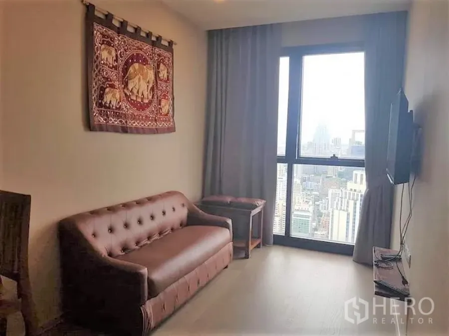 Condominium for rent in Watthana, Bangkok - Living room with wall-mounted TV, sofa and floor-to-ceiling city view window.