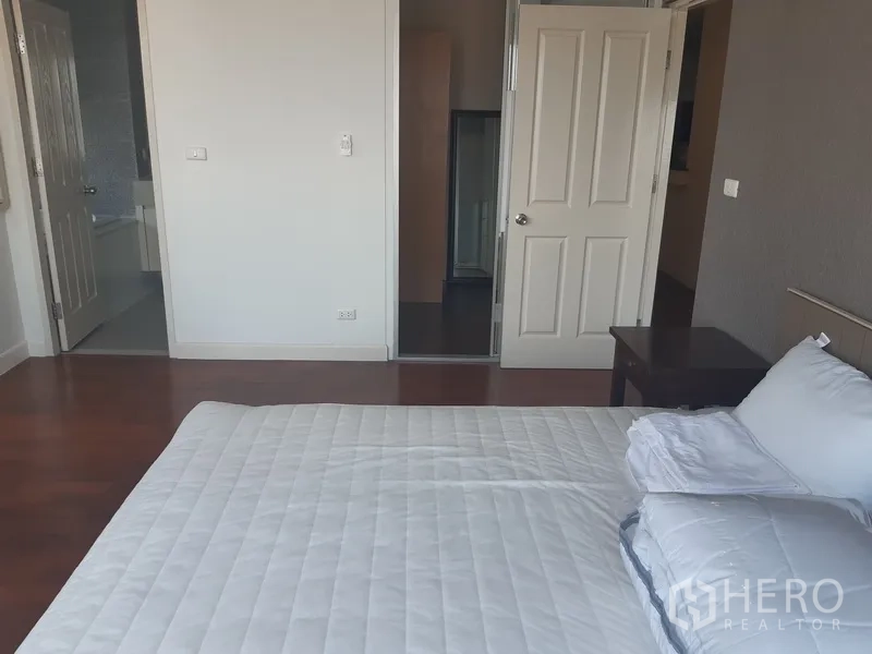 Condominium for rent in Khlong Toei, Bangkok - Master bedroom facing hallway and ensuite entrances with warm wood flooring.