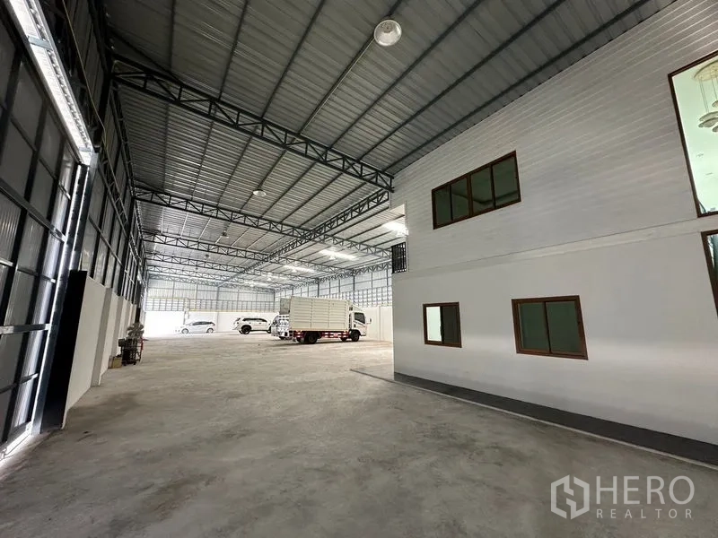 Warehouse for rent in Lam Luk Ka, Pathum Thani - Spacious warehouse interior with high steel truss roof and attached two-storey office block.