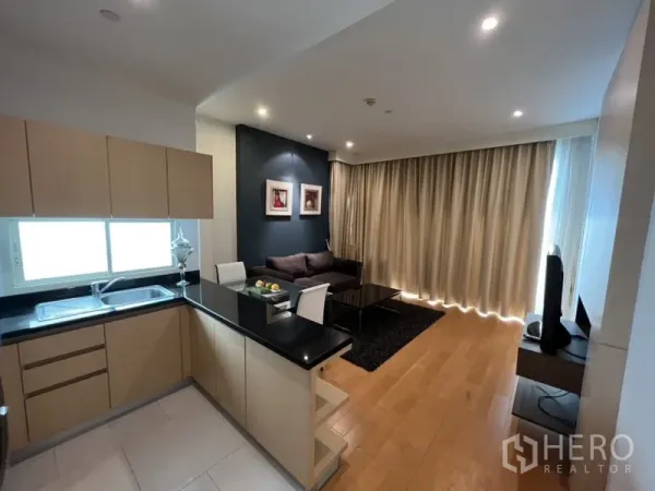 Condominium for rent in Chatuchak, Bangkok - L-shaped kitchen with black countertops overlooking living area with full-length curtains.