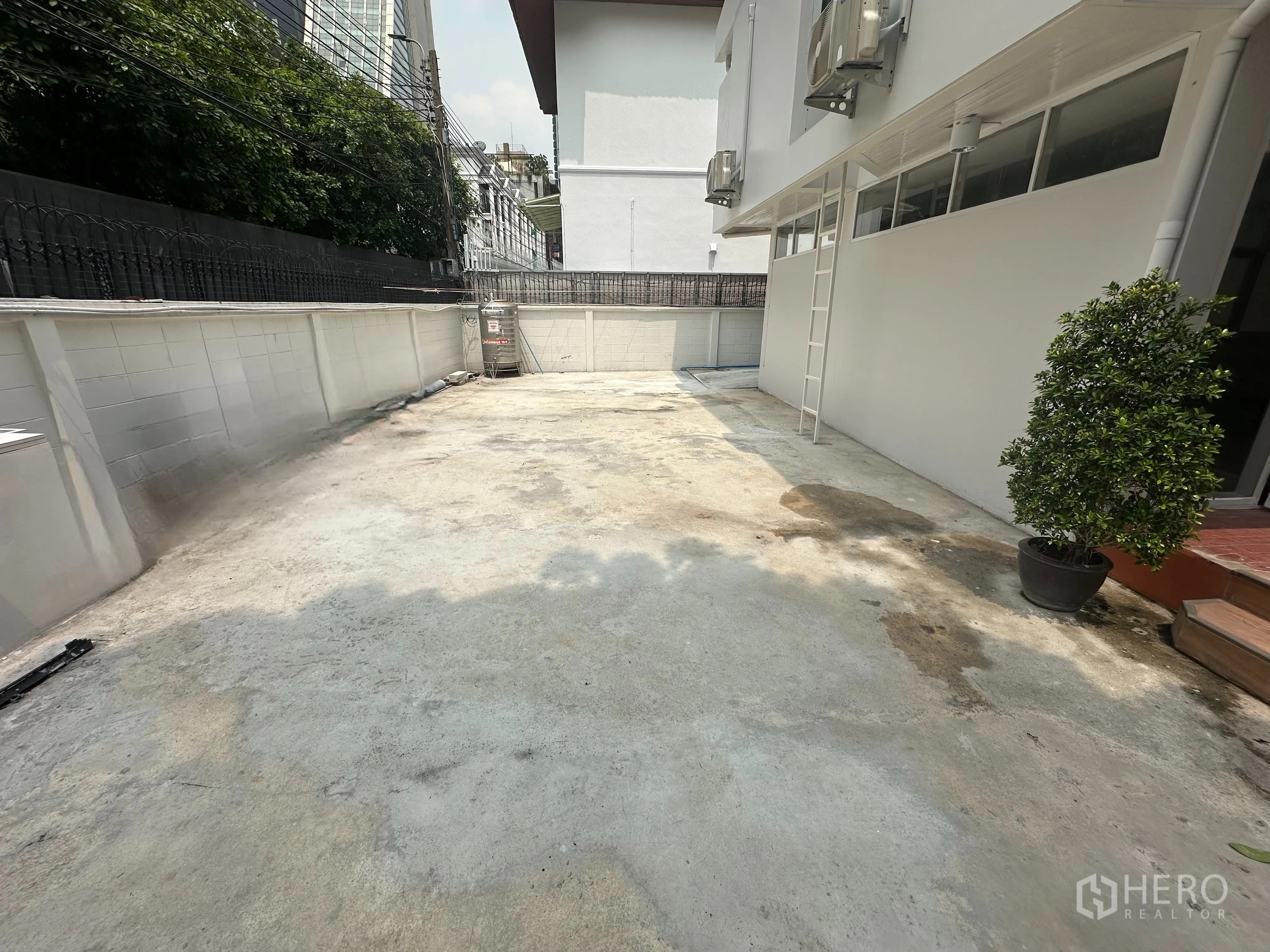带办公室的家 出租在Watthana, Bangkok - 建筑侧面宽阔的混凝土庭院与车道，围墙与外挂机组可见。