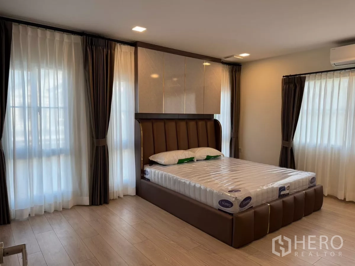 独立式住宅 出租在Bang Phli, Samut Prakan - 主卧配软包大床，宽大窗户，纱帘与遮光帘，木纹地板。