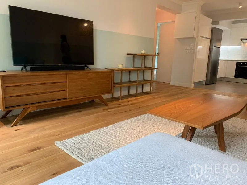 Condominium for sale in Watthana, Bangkok - Living room media unit and coffee table on wood flooring near the kitchen.
