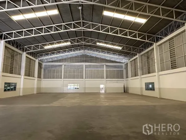 Factory for rent in Samut Prakan - Spacious warehouse interior with high steel truss roof, concrete floor and ample lighting.