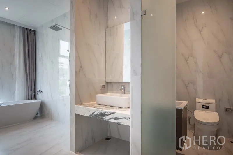 Condominium for rent in Khlong Toei, Bangkok - Modern marble bathroom with large mirror, rain shower and freestanding bathtub by the window.